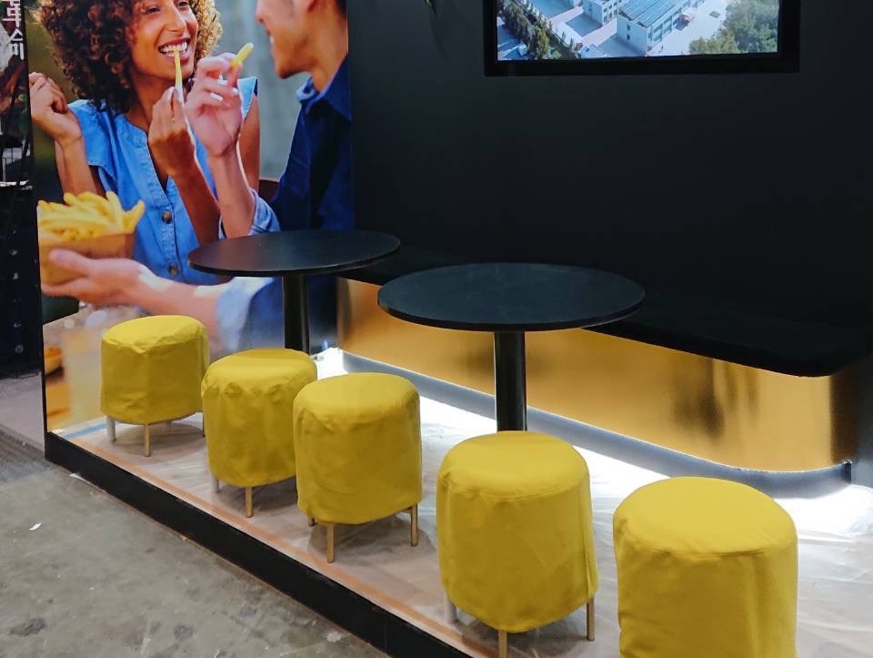 展示会ブースのテーブルまわりに並んだ、からし色の布で覆った丸いスツール